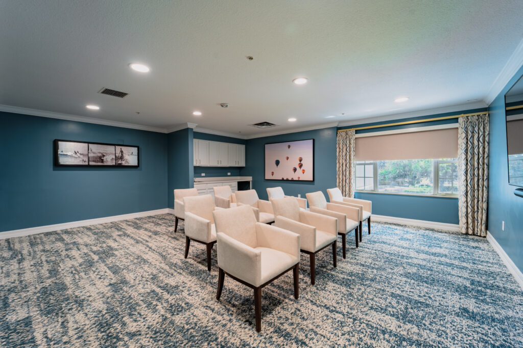 MemC 27 of 52 - Ambiance at Maitland Blue-walled theater room with comfortable white chairs provides entertainment space for memory care residents near Longwood FL.