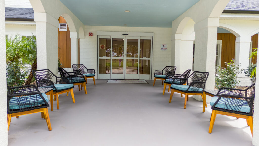 Modern wicker chairs arranged in a covered entrance area create an inviting welcome for assisted living visitors near Winter Park FL.